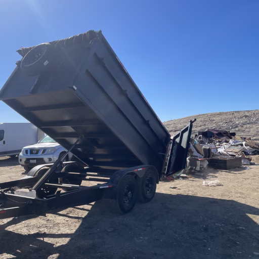 OC Bros team performing Orange County junk removal at landfill, unloading furniture, wood, and household debris from dump trailer