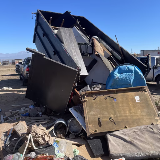 Orange County junk removal crew unloading mixed debris and furniture OC Bros trailer unloading mixed junk and debris at a Southern California dump site — furniture, construction materials, and household items being properly disposed of.